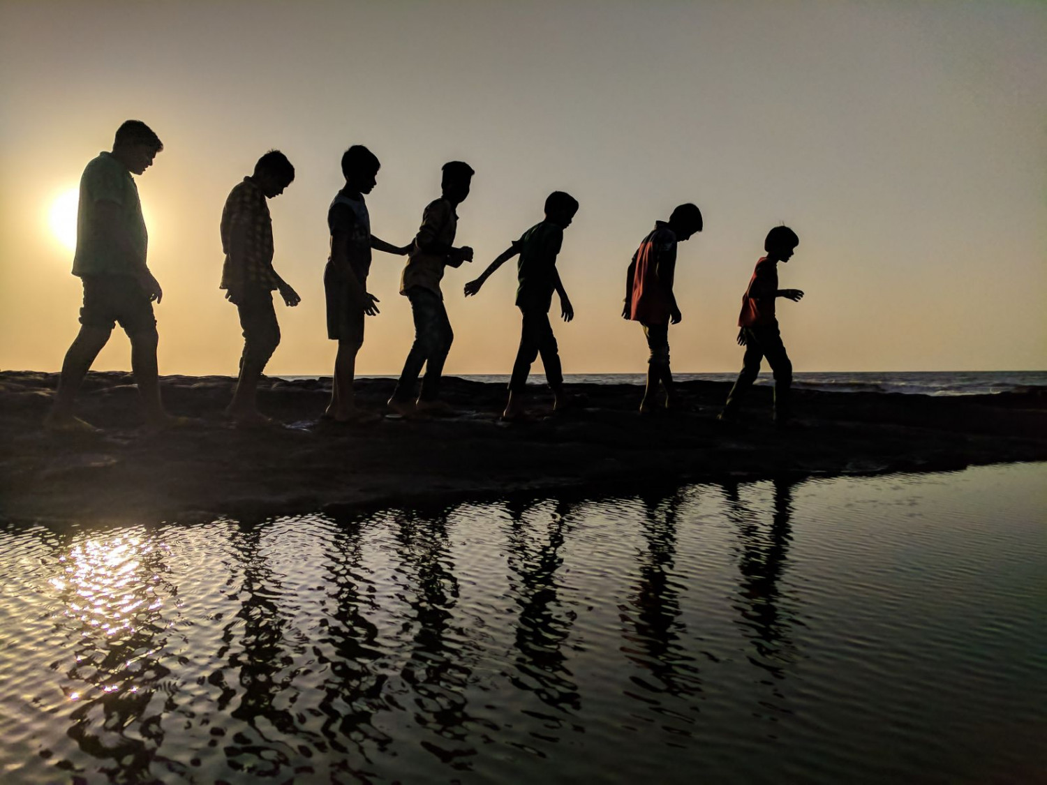 Children approaching the water's edge during sunset