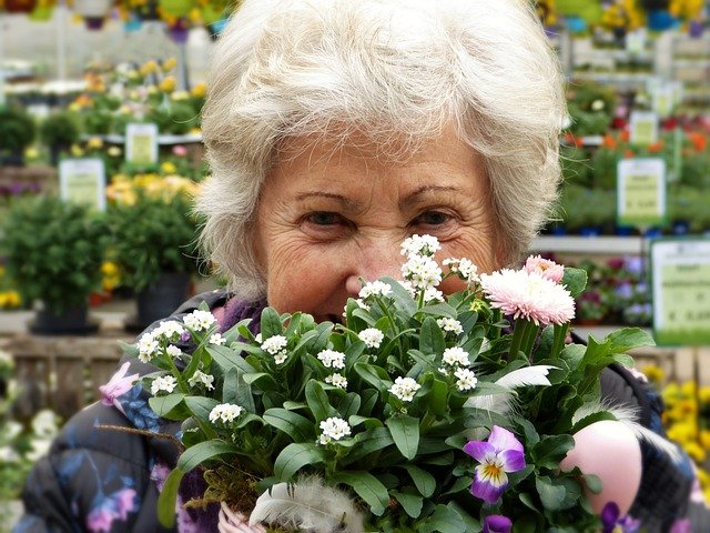 An older woman hiding behind a bunch of flowers
