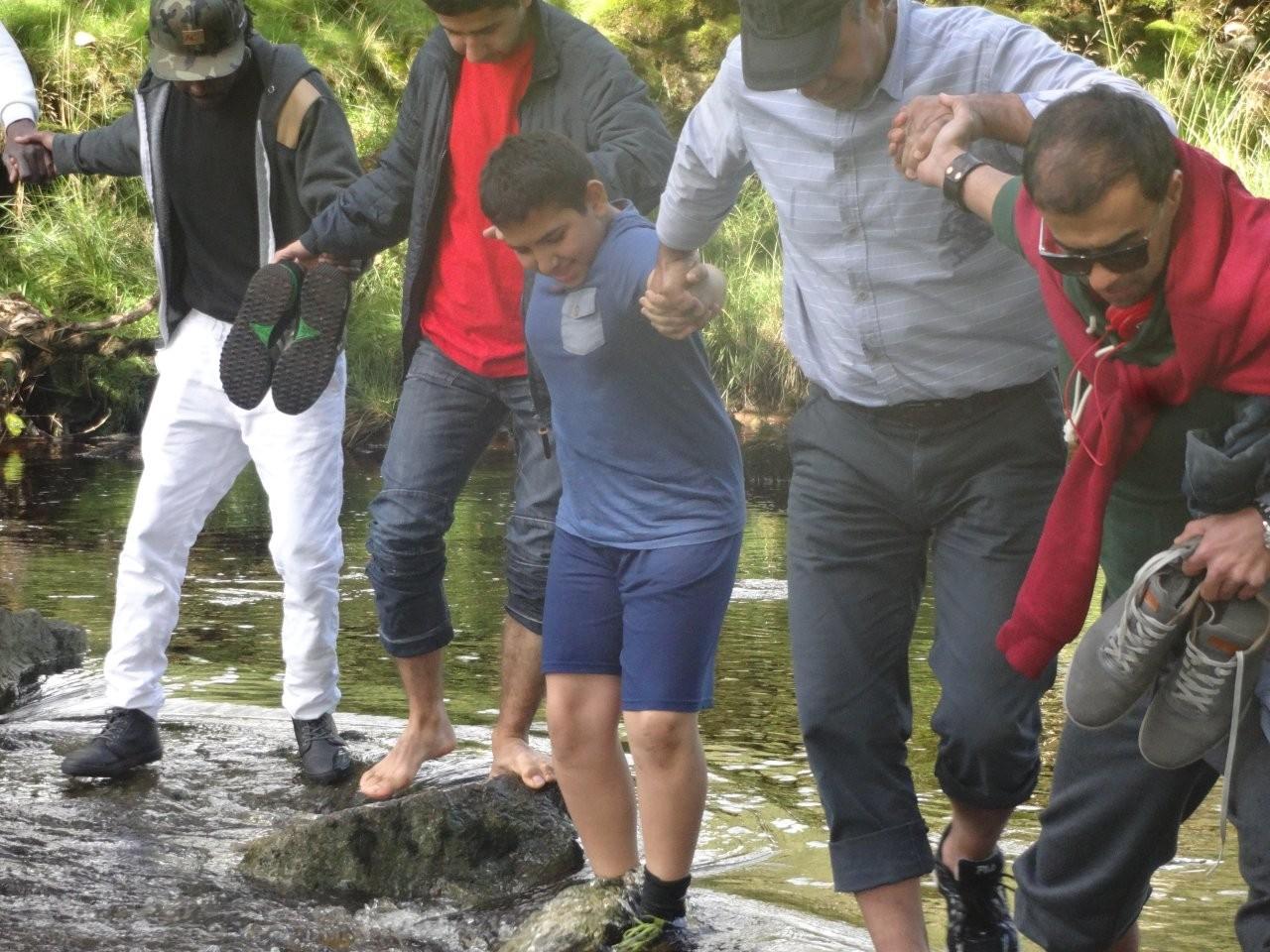 A group of refugees helping each other to cross the river